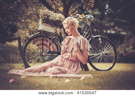 Dreaming blond retro woman with a book in summer dress sitting on a meadow