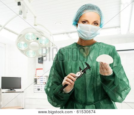 Plastic surgeon woman with silicon breast implant and calliper in surgery room interior 