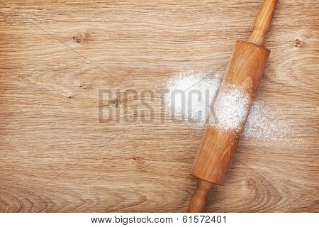 Rolling pin with flour on wooden table. View from above