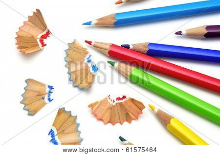some colored pencils of different colors and pencil shavings on a white background