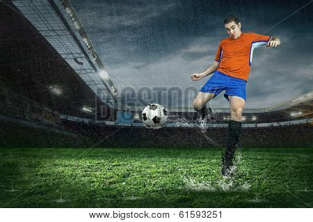 Football player with ball in action under rain in stadium