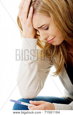 Sad young woman holding pregnancy test feeling hopeless