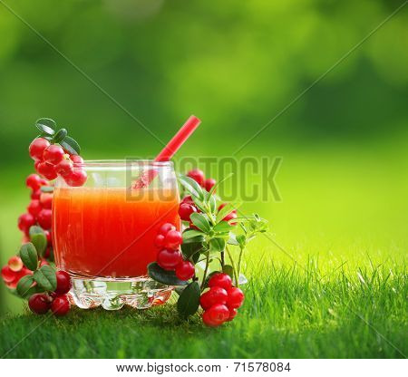 Berry juice and forest cowberry with leaves against blurred green background.