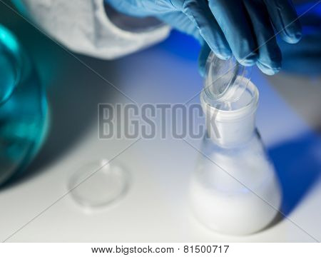 science, chemistry, biology, medicine and people concept - close up of scientist hand pouring chemical powder into flask making test or research in clinical laboratory