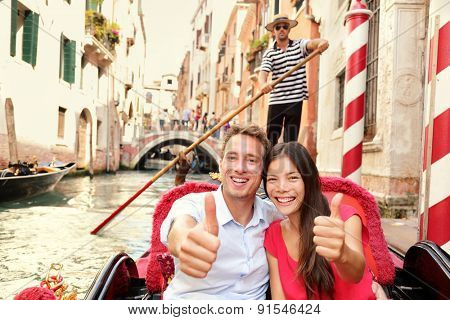 Tourists happy couple traveling in Venice gondola giving thumbs up hand sign joyful on travel. Romantic young beautiful couple on vacation holidays sailing in venetian canal in gondole. Italy