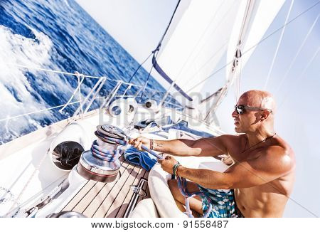 Handsome man working on sailboat, pulling rope, active summer vacation on water transport, having fun in the sea, enjoying water sport