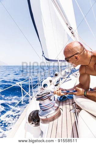 Handsome man working on sailboat, pulling rope, active summer vacation on water transport, having fun in the sea, enjoying water sport