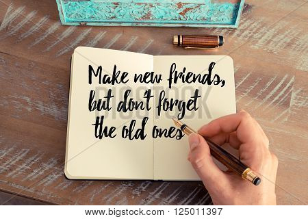 Retro effect and toned image of a woman hand writing on a notebook. Handwritten quote Make new friends, but don't forget the old ones as inspirational concept image