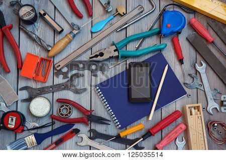 Notepad mobile phone and tool scattered around him on the wooden floor top view. Locksmith and carpentry tools.