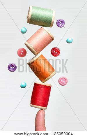 Spools of thread balancing on a finger and buttons flying in the air.