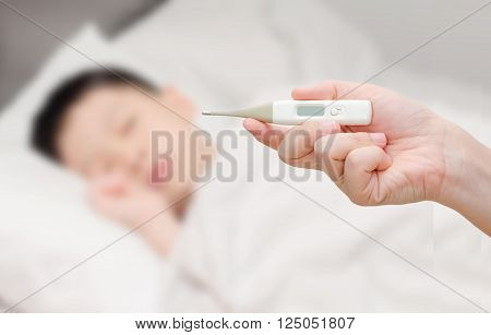 Mother 's hand holding digital thermomether with sick boy in background