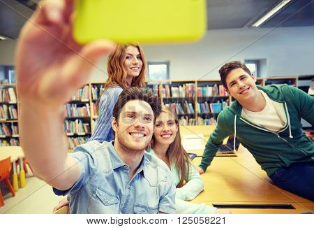 people, technology, education and school concept - happy students or friends with smartphone taking selfie in library