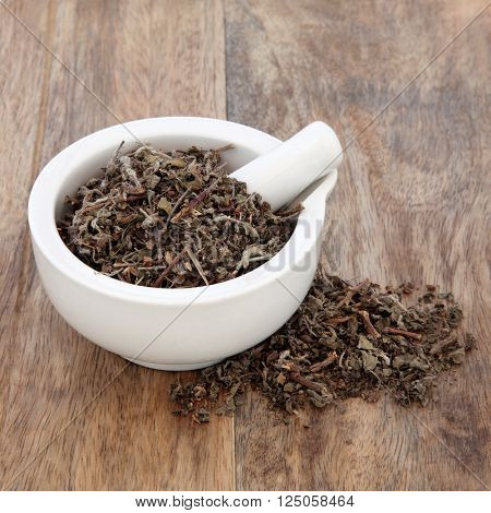 Tulsi holy basil herb used in natural alternative herbal medicine in a mortar with pestle over old wooden background.
