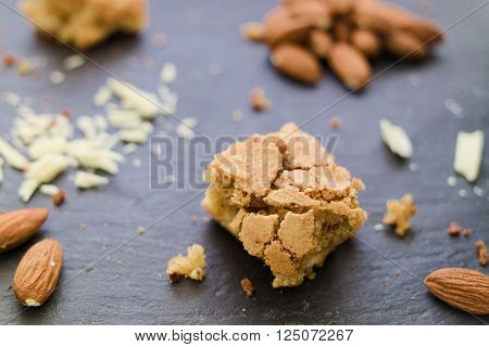 White chocolate and almond brownie on dark background. White chocolade whole almonds and crumbles. Selective focus.
** Note: Shallow depth of field