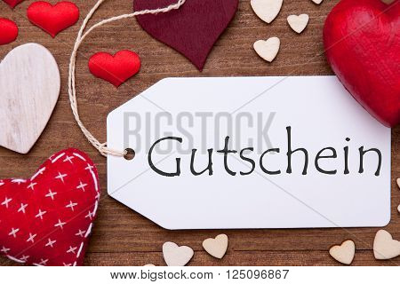 Label With Red Textile Hearts On Wooden Gray Background. German Text Gutschein Means Voucher. Retro Or Vintage Style. Macro Or Close Up Of One Label