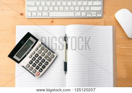 Top view workspace with blank notebookpencalculator keyboard and mouse on wooden table background.