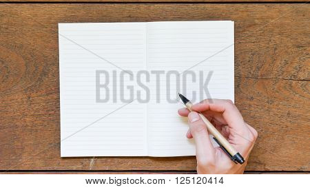 Man hands with pen writing on empty notepad over wooden table.
