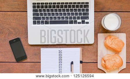 Laptop, notebook, mobile phone and breakfast on wooden table background.