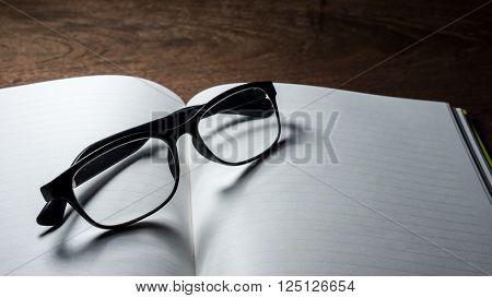 Blank notebook with glasses on wooden table.