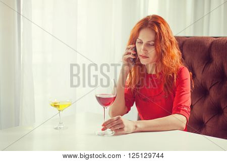 Beautiful girl talking on the phone in a cafe and drink wine.