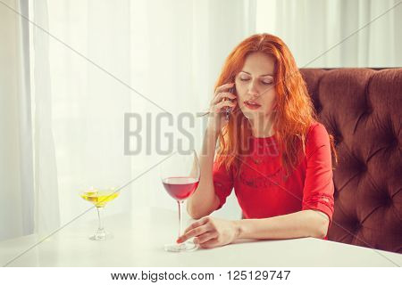 Beautiful girl talking on the phone in a cafe and drink wine.