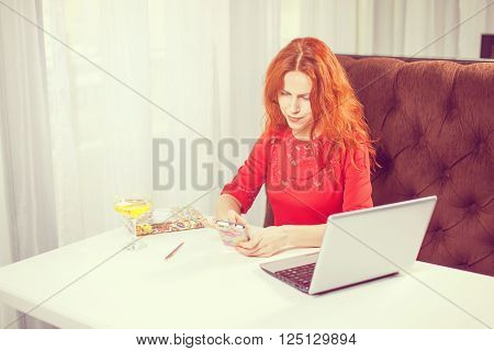 Happy entrepreneur working with a phone and laptop in a coffee shop.