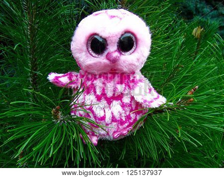 Pink plush owl sitting on a pine tree