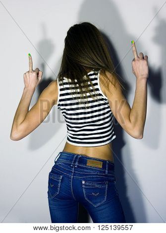 sexy blonde girl in jeans and striped t-shirt, turned his back and raised both hands up, showing middle finger.