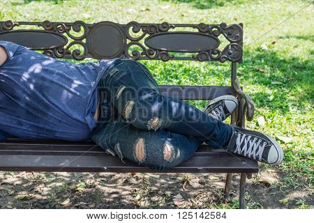 Homeless man is sleeping on a bench in the park.