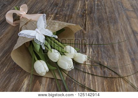 Bouquet of fresh white tulips and decorative butterfly on wooden rustic background.