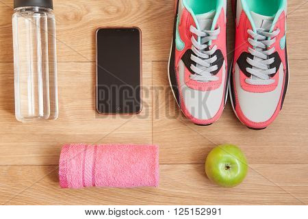 red and grey sneakers with grey shoelaces and red towel green apple bottle with water mobile phone on wooden background indoors