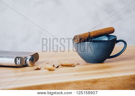 Tabletop with cigar on top of coffee cup silver flask and filing on concrete background