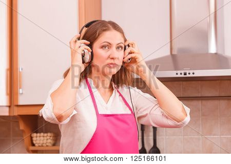Cooking preparing and making food concept. Modern beauty woman housewife cook chef wearing pink apron and listening music on earphones standing in kitchen.