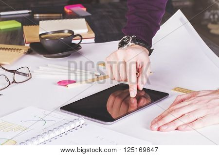 Male hand using tablet placed on large whatman with office tools