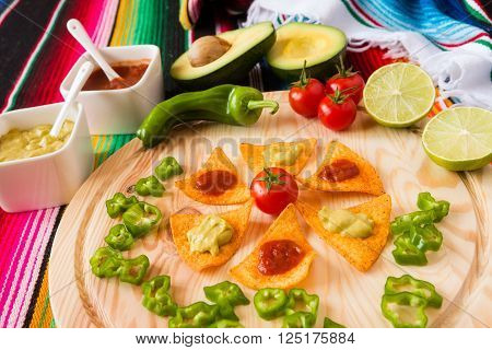 Nachos chips and vegetables on a chopping board over a colored poncho