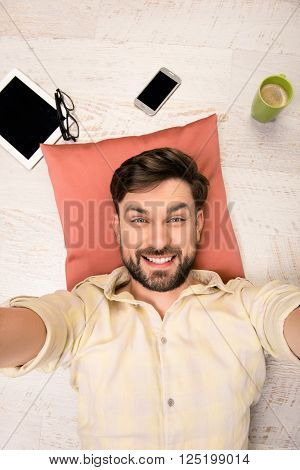 Handsome Man Lying On The Floor On Pillow  And Making Selfie