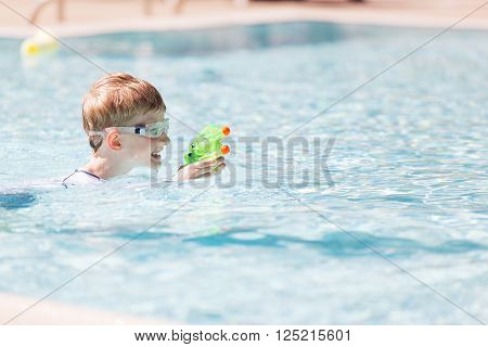 smiling excited boy with beach toy in goggles and rashguard enjoying warm weather in swimming pool vacation and sun protection concept