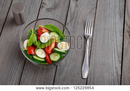 Salad with spinach leaves, tomato, cucumber and quail eggs in glass bowl on a wooden rustic table, top view with copy space. Healthy food