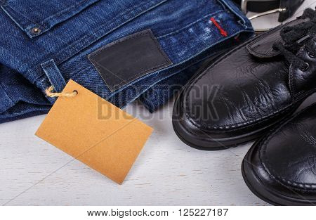 Set of men's clothing shoes jeans and a belt with blank tag on white wooden background top view