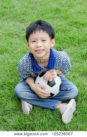 Young asian boy with ball sitting on grass field