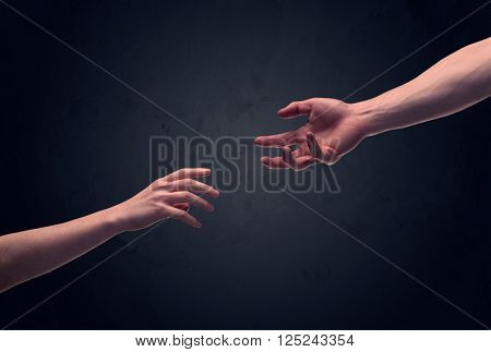 Two male hands reaching out to one another, almost touching, in front of dark clear empty background wall concept