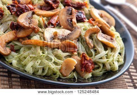 Italian Linguini pasta with pesto and mushrooms in a dark plate. Close up