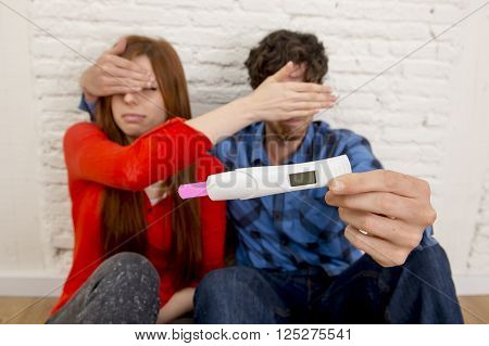 young sad couple in shock and surprise holding pink positive pregnancy test blocking eyes scared to confirm that the girl is pregnant in unexpected baby and parenthood concept