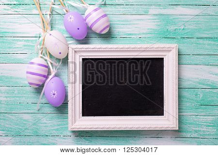 Easter or spring background. Decorative violet eggs and empty blackboard on turquoise wooden background. Selective focus. Place for text.