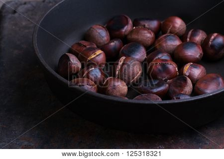 Roasted chestnuts in a pan on wooden background