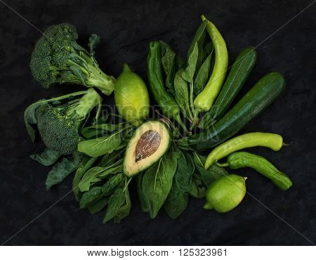 Raw green vegetables set. Broccoli, avocado, pepper, spinach, zuccini and lime on  dark stone background, top view