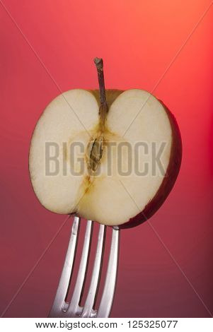 Red apple cut in half on fork with color background concept photo. Ideal for healthy eating campaign or fitness poster.