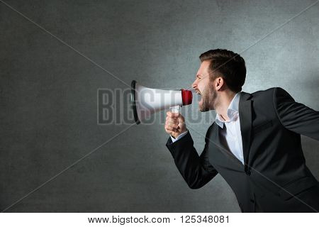 Young handsome shouting man using megaphone over grey background