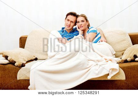 Smiling loving couple sitting on couch with blanket
