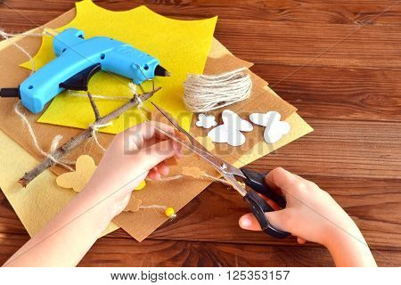 Child holds the scissors and cut out the felt flower. Scissors, hot glue gun, sheets of felt, decorative pendant with felt butterflies and flowers